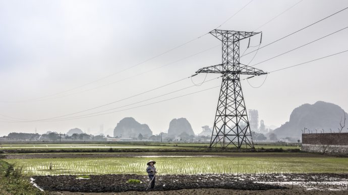 Ninh Binh, Vietnam - March 4, 2016: A farmer is working on the field at Ninh Binh, Vietnam. In the background is a  High-voltage line and the famous rocks of Ninh Binh.